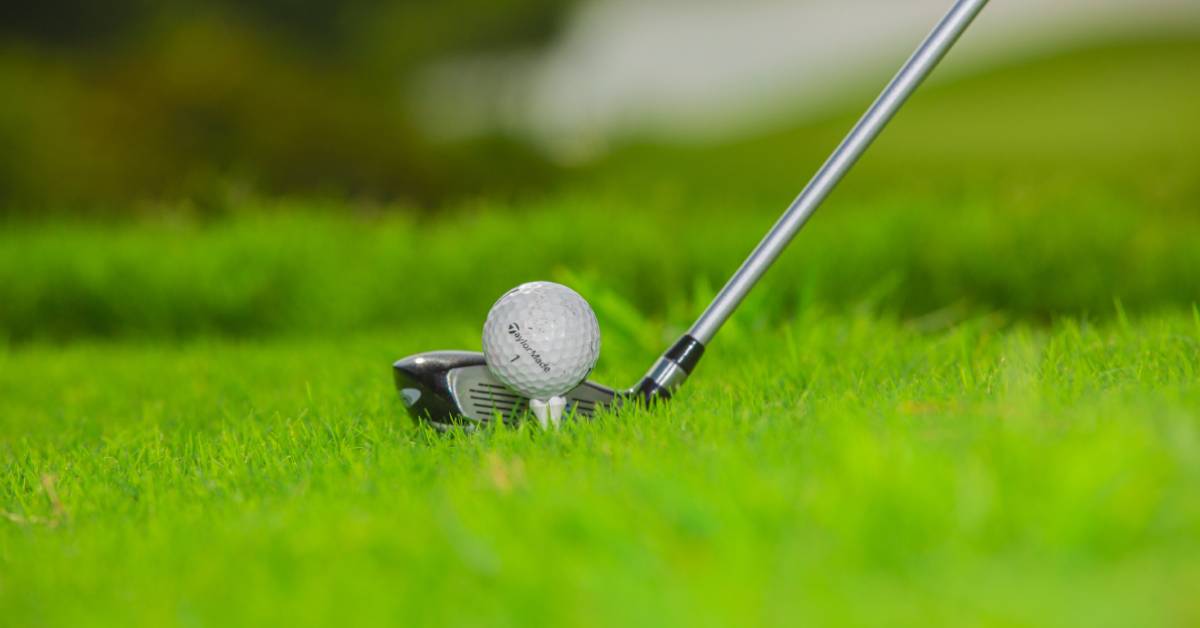 A golf ball on the tee with a club positioned for a swing on a green course.