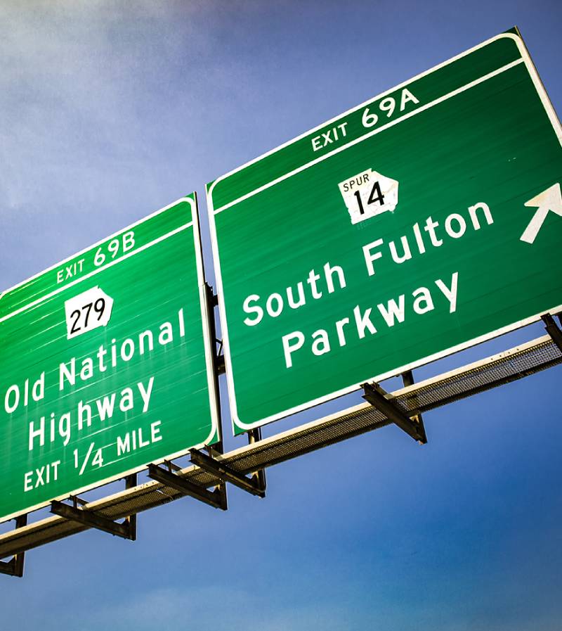 Two green highway exit signs against a blue sky, one pointing to Old National Highway and the other to South Fulton Parkway.