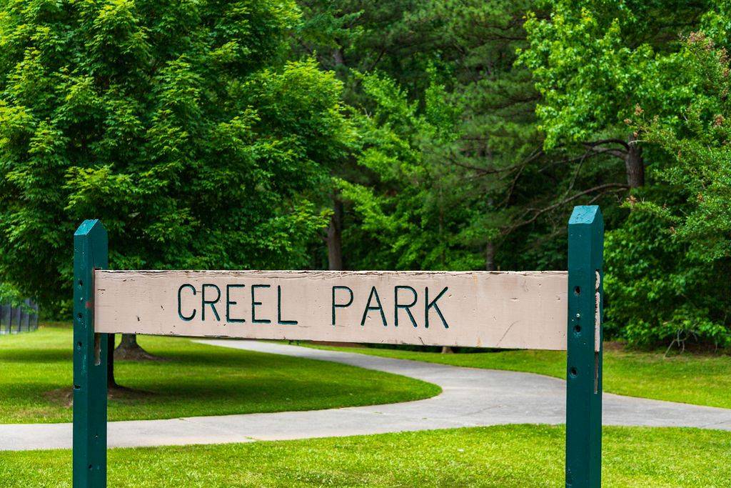 Wooden-sign-reading-_CREEL-PARK_-with-pathway-and-lush-green-trees-in-the-background
