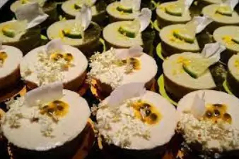 A variety of mini cakes featuring creamy layers, topped with coconut shavings and fresh fruit slices, beautifully arranged